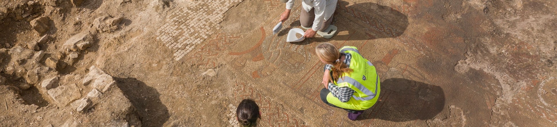 Archaeologists excavating a Roman Mosaic with human figures and a decorative border.