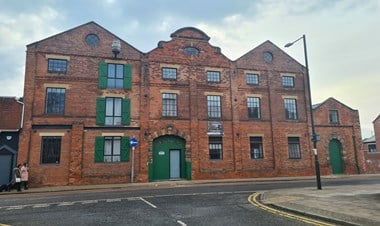A colour photo of a 4-storey red brick industrial building with green shutters and doors.