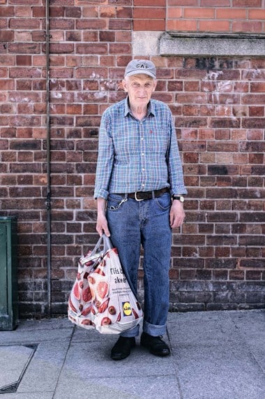 Colour photo portrait of a man standing with shopping bags on a pavement.