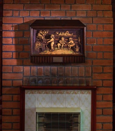 A brick chimney breast with tiles surrounding a gas fire. A relief of bathers enjoying a sauna hangs above it. 