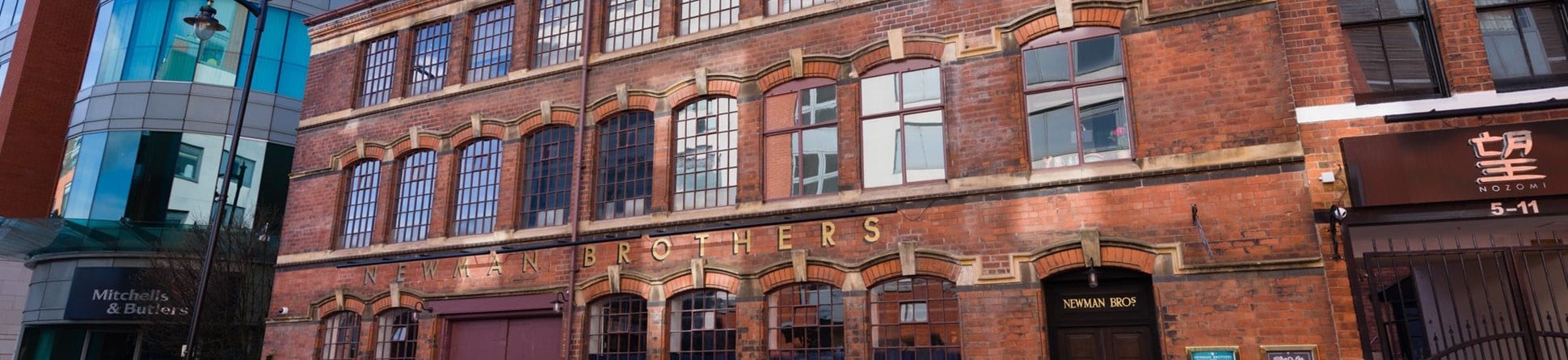 Landscape photograph of the front exterior of the Coffin Works, which is a three story red brick Victorian building with 'Newman Brothers' in gold lettering just above the ground floor