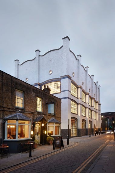 A photograph of a street scene featuring a pub and a white brick office building with large, latticed windows lit up at dusk
