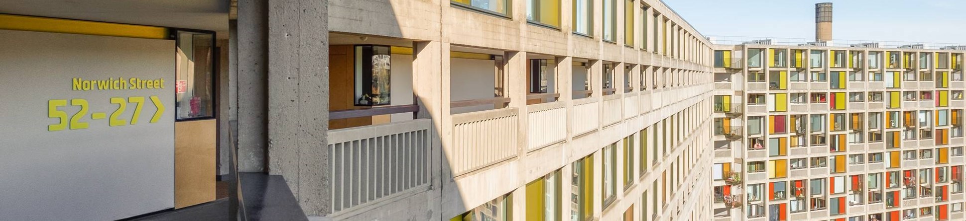Phase 1 of Park Hill showing ‘streets in the sky’ corridor and external view of refurbished building façade. The facade displays the original concrete framing and bold coloured panels next to the windows.  