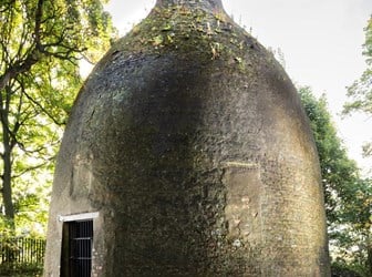 A brick bottle-shaped structure situated in a wooded area.  