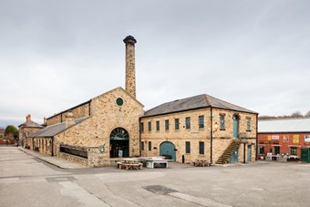 Two-storey light brick industrial buildings with concrete paved foreground.