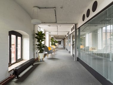 An office corridor with glass-fronted meeting rooms on the righthand side.