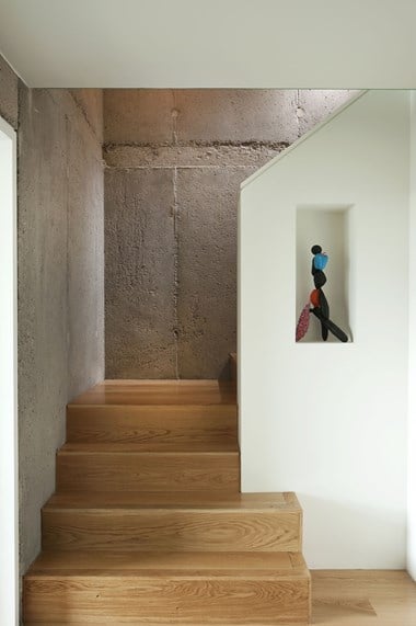 A photo of a small interior wooden staircase, with a low ceiling above and a concrete wall in the background
