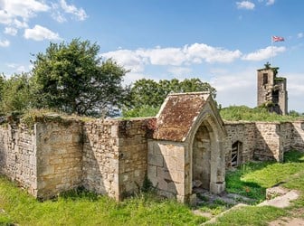A general view of a stone priory ruins, flying a union jack flag in the background from a tower, or higher part of the priory. 