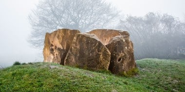 A structure made of large sarsen stones is visible through the mist. 