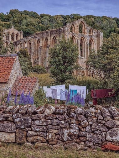 A photograph of abbey ruins with hanging clothes washing and a dry-stone wall in the foreground.