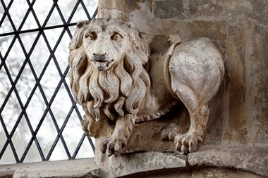 Stone carving of a lion on an interior wall next to a leaded window.