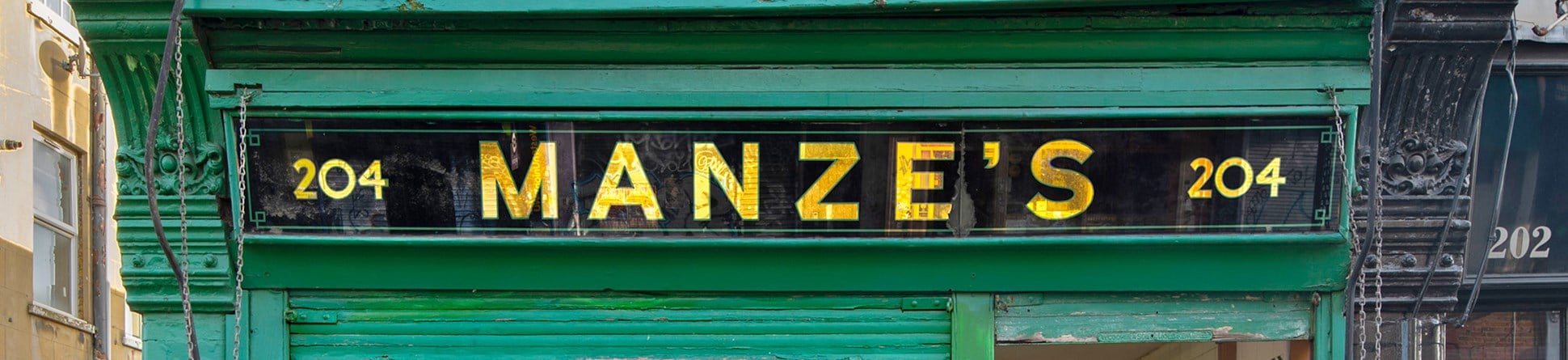 A green shop front with a sign saying "204, Manze's, 204; Meal in a moment, Manze's Meat Pies, all made daily".