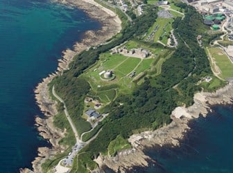 An aerial photograph of a rocky headland with a large complex of historic buildings at its centre.