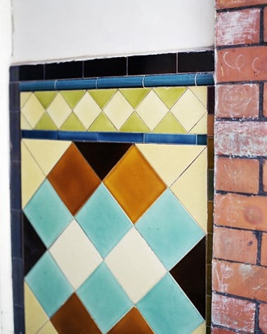 Panel of glazed tiles with brick wall running up right edge.