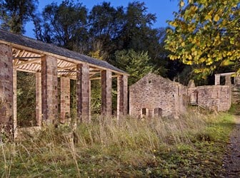 A ruined stone industrial building with modern stone structure in the foreground.