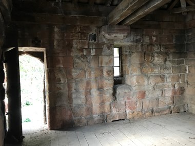 The interior of a stone building, with dusty floorboards and a packed-earth floor. 
