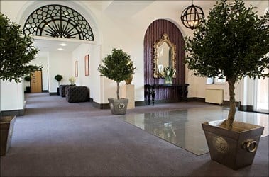 A photograph of an entrance lobby with purple carpet, white walls, plants in pots and other decorative ornaments