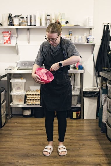 Portrait of a woman in a commercial kitchen mixing cake mixture in a bowl.