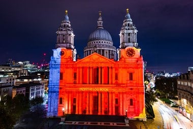 The Where Light Falls title projection sets the west elevation of St Paul's ablaze in red with the poem title 'FROM THE LOG BOOK' visible in yellow between the two floors of columns.