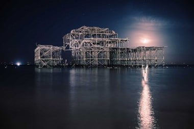 A moonlit photograph of the remains of a large pier structure and water in the foreground.