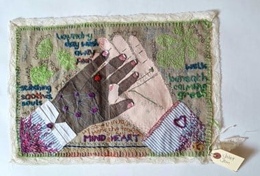 Fabric with white and coloured hands entwined with words embroidered on it.