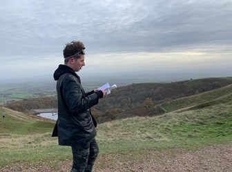 A young man studying information whilst visiting a hillfort; a landscape of fields is in in the background.