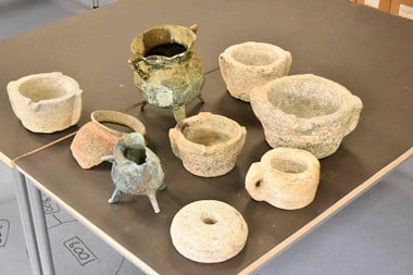Cauldrons, cups, pottery and kitchen objects from a wreck site laid out on a table