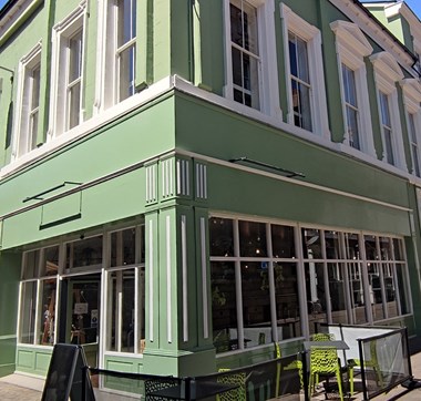 A sage green painted cafe front with smart chairs outside and elegant architectural flourishes.