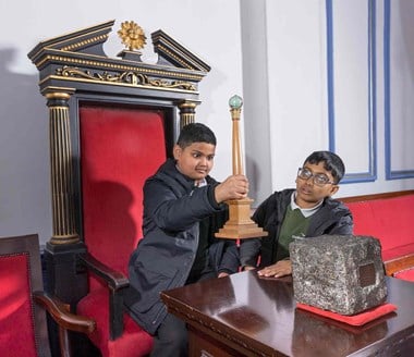 Two school boys with one of them sitting on a large chair holding up masonic artefact