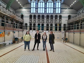 A group of young people standing in the dry pool of a historic Victorian municipal baths building.