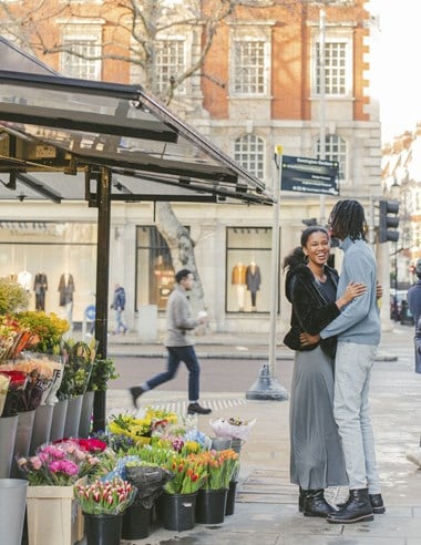 A couple embracing beside a florist's stall on the corner of a London street.
