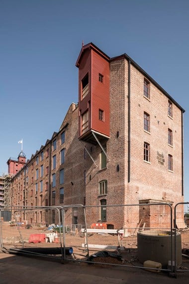 A five storey brick warehouse type building with security fencing and building materials in the foreground.