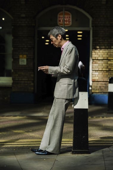 A portrait of a man wearing a suit, leaning against a bollard.