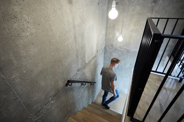 A man walking down an internal staircase surrounded by black railings and a bare concrete wall