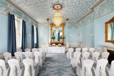 An interior photograph of white chairs and a table set up for a wedding registry ceremony in a light blue, decorative, Georgian-era function room