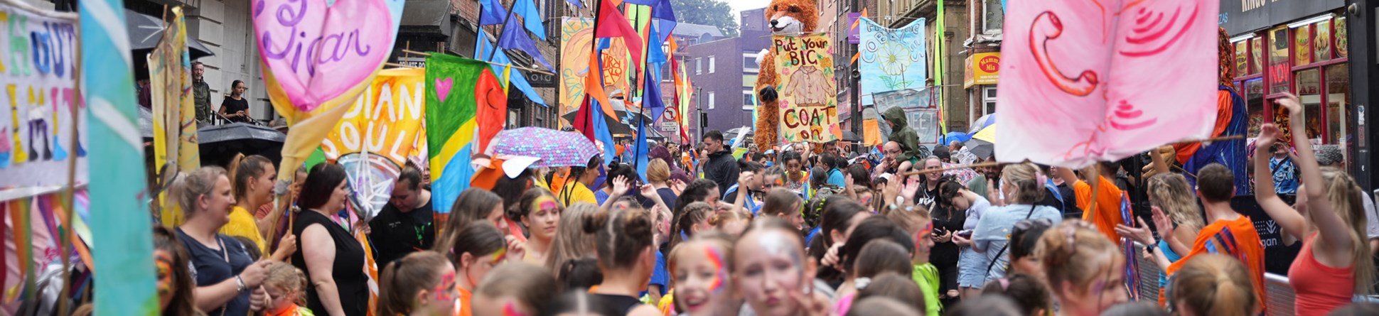 A tightly packed crowd of people with colourful banners and face paint. In the background a large fox puppet towers above the crowd.