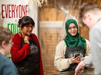 Young people wearing "People-powered press" aprons set letters on a large wooden printing dye