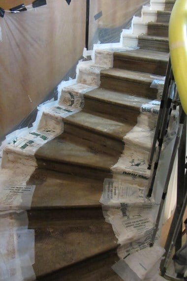 A stone staircase with paint removal sheets on the sides and a wall covered in plastic sheeting.