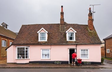 Pink cottage with postman and trolley standing at the front door.