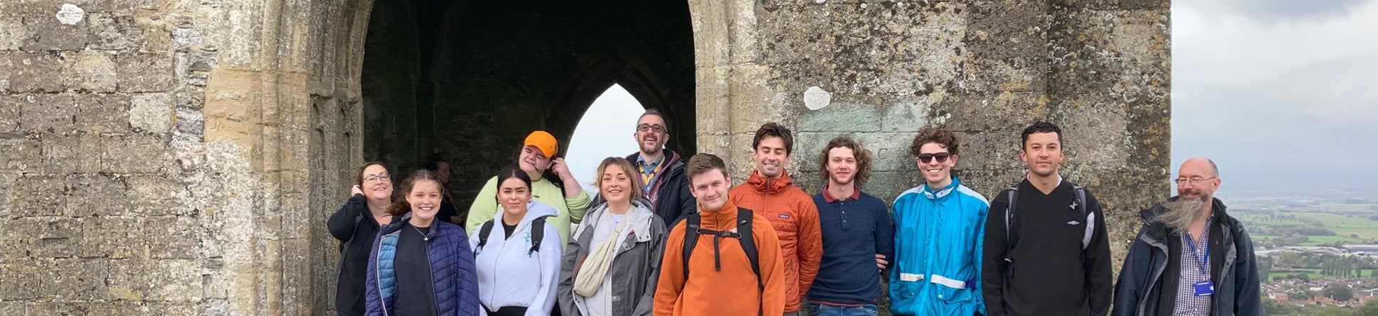A group of smiling people posed in front of the archway of a church atop a tor.